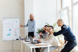 A group of professionals engaged in a business meeting, discussing financial graphs on a whiteboard.